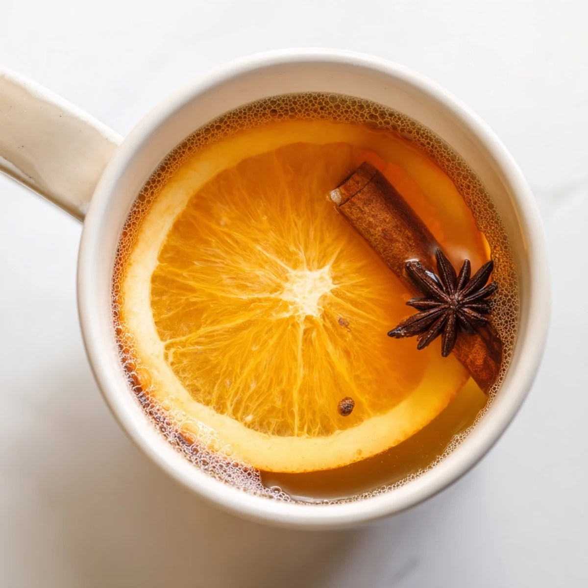 Close-up view of Spiced Apple Cider with Orange Slices simmering in a pot, featuring whole star anise and cloves floating in the rich, amber liquid.