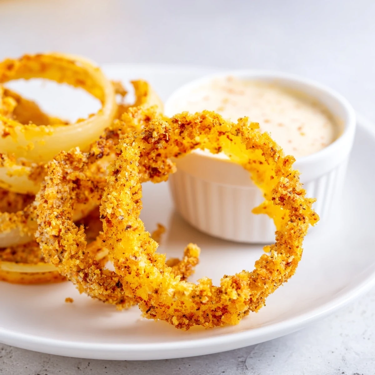 A hand holding a crunchy panko-crusted air fryer onion ring ready to be dunked in creamy burger sauce.