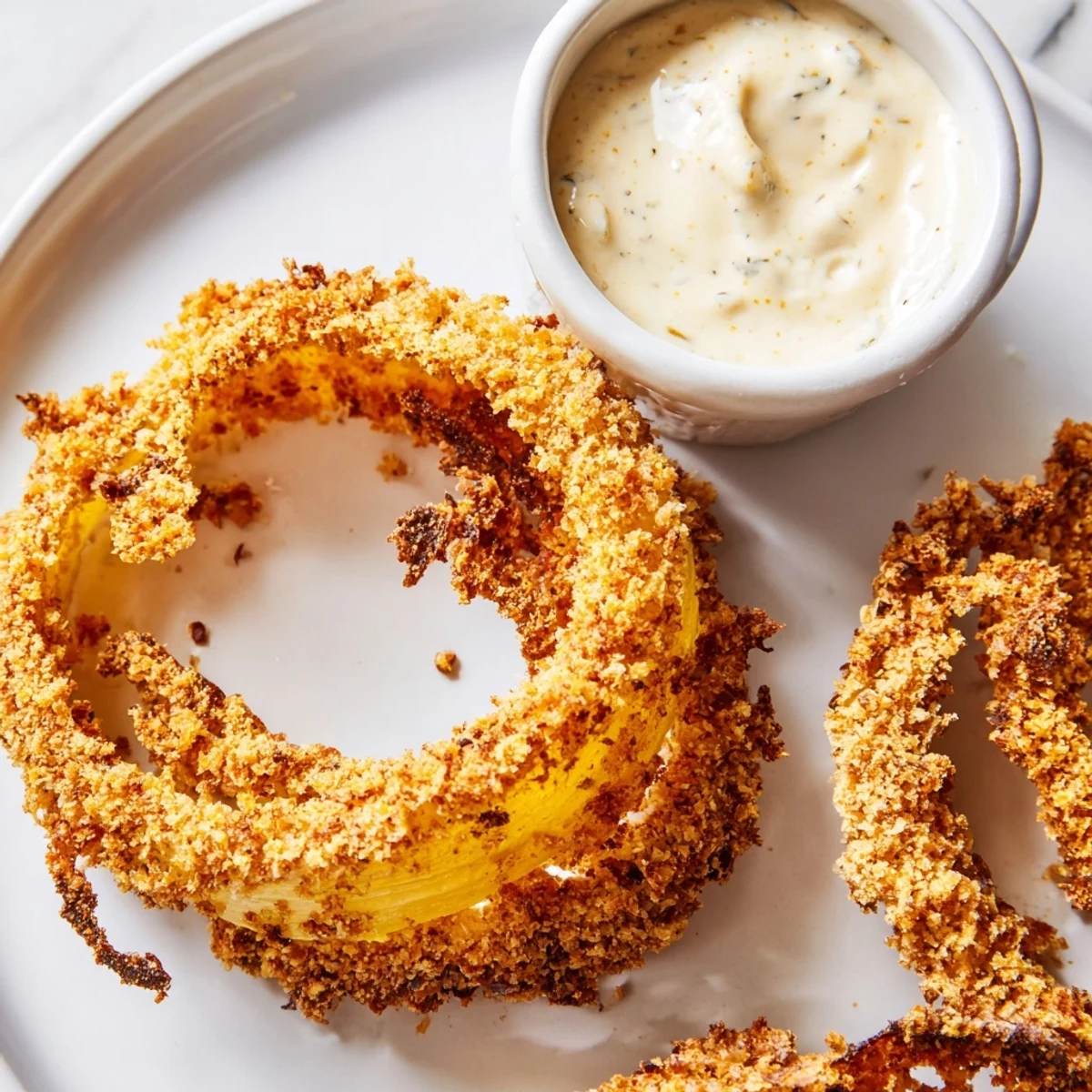 Sizzling golden air fryer onion rings served hot alongside a dipping bowl of ketchup-mustard burger sauce.