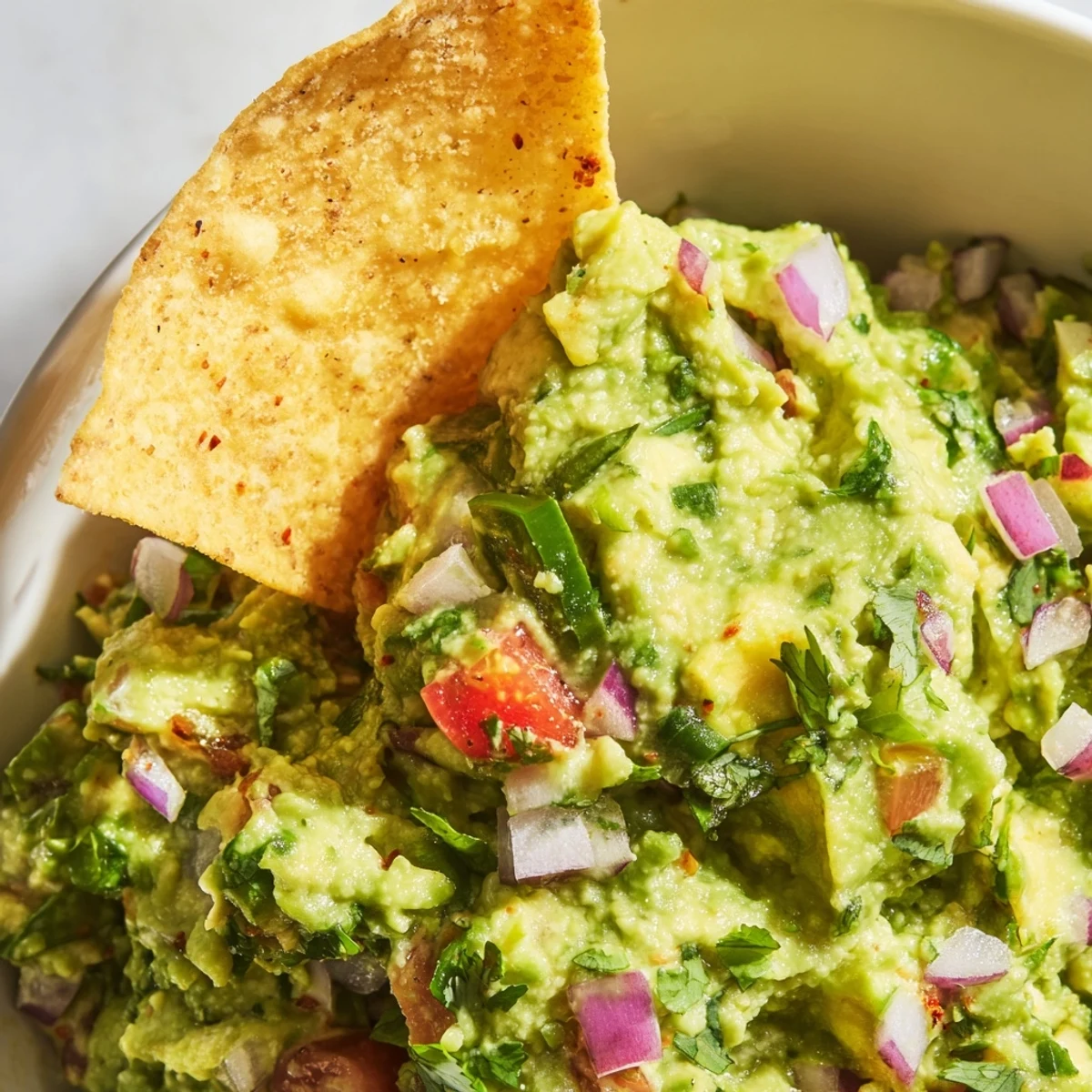 Freshly baked golden tortilla chips sit beside a vibrant bowl of Big Game Guacamole, garnished with cilantro and jalapeños.
