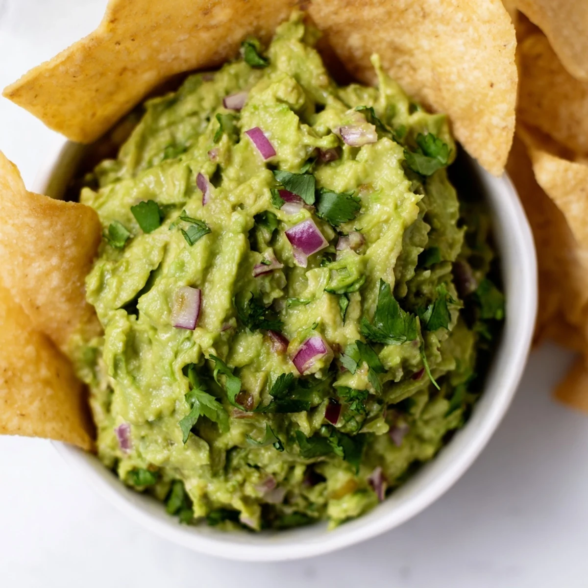 Bright green, chunky Game Day Spicy Guacamole with Tortilla Chips in a rustic bowl, surrounded by fresh avocado halves and lime wedges.