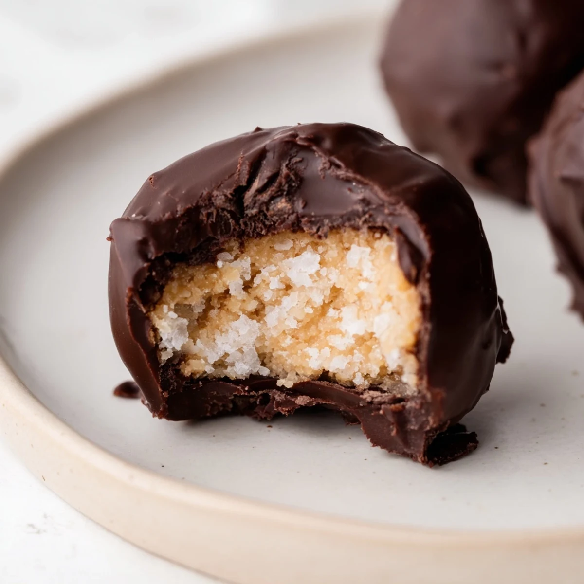 A close-up view of chocolate peanut butter balls arranged on a baking sheet lined with parchment paper, showing slight cracks in the rich dark chocolate coating from the chilling process.