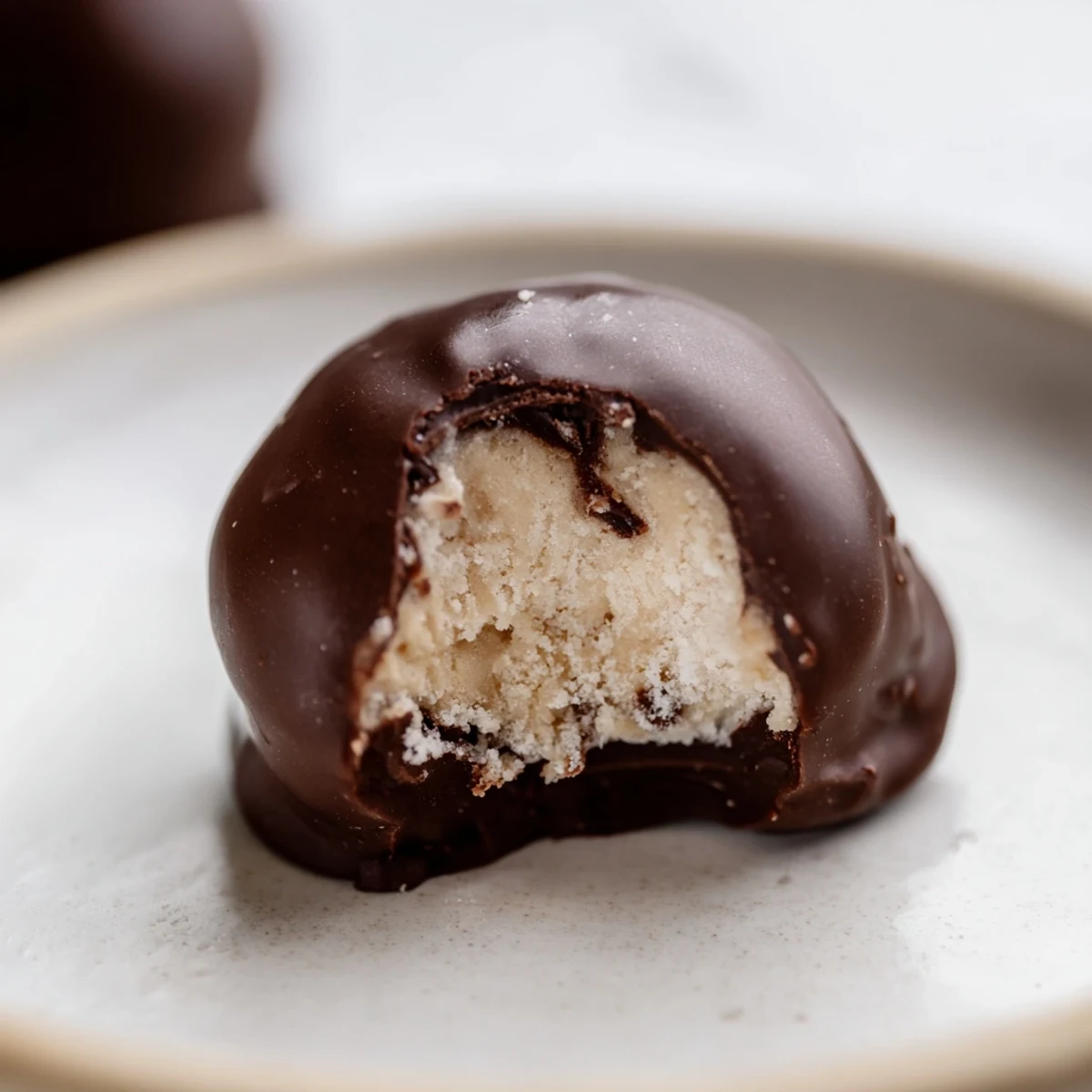 Chilled chocolate peanut butter balls are arranged on a silver serving platter, accompanied by a small glass bowl of peanut butter and a dusting of powdered sugar.