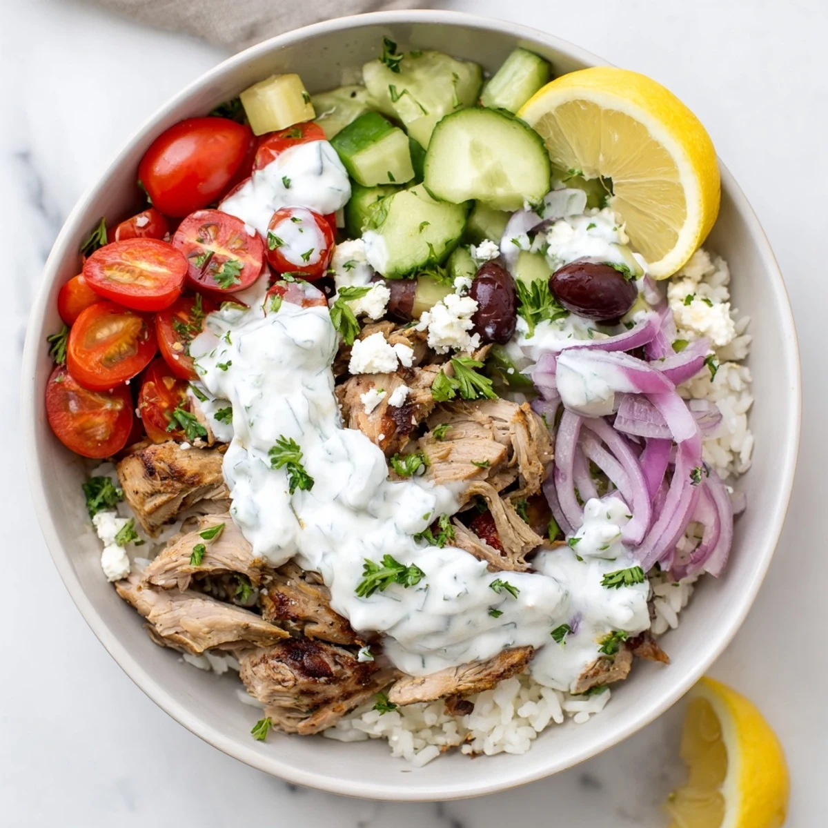 Hearty Greek Chicken Gyro Bowls with Tzatziki are plated with juicy chicken, crisp cucumbers, and a generous drizzle of creamy yogurt sauce.