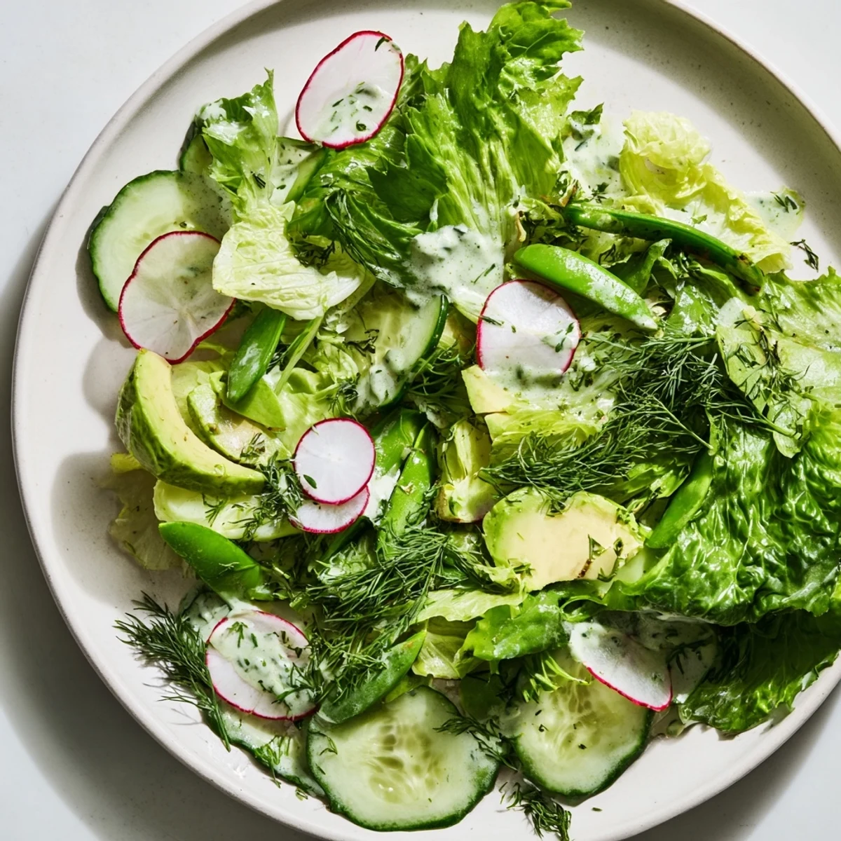 Bright green Green Salad with Green Goddess Dressing topped with creamy avocado and crisp radish slices, served fresh and vibrant.