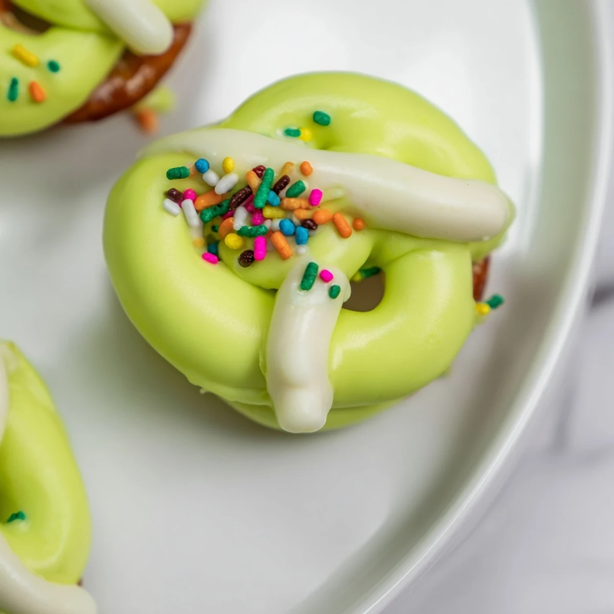 A close-up of pretzel treats with green chocolate drizzle, showing glistening melted chocolate over crunchy, golden-brown pretzels.