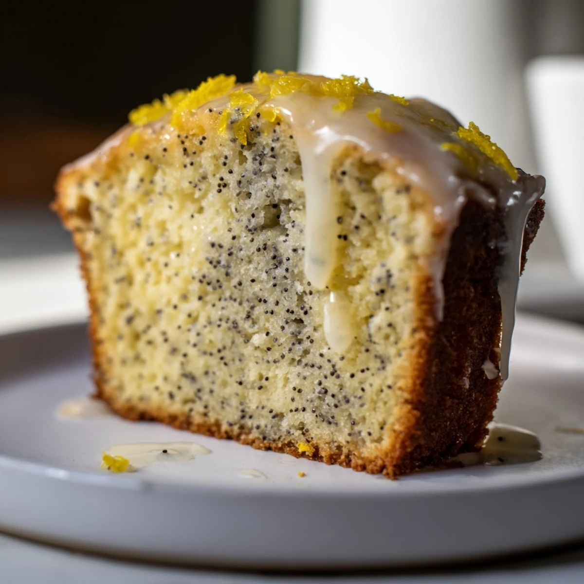 A moist slice of Lemon Poppy Seed Loaf topped with fresh lemon zest and a white plate.