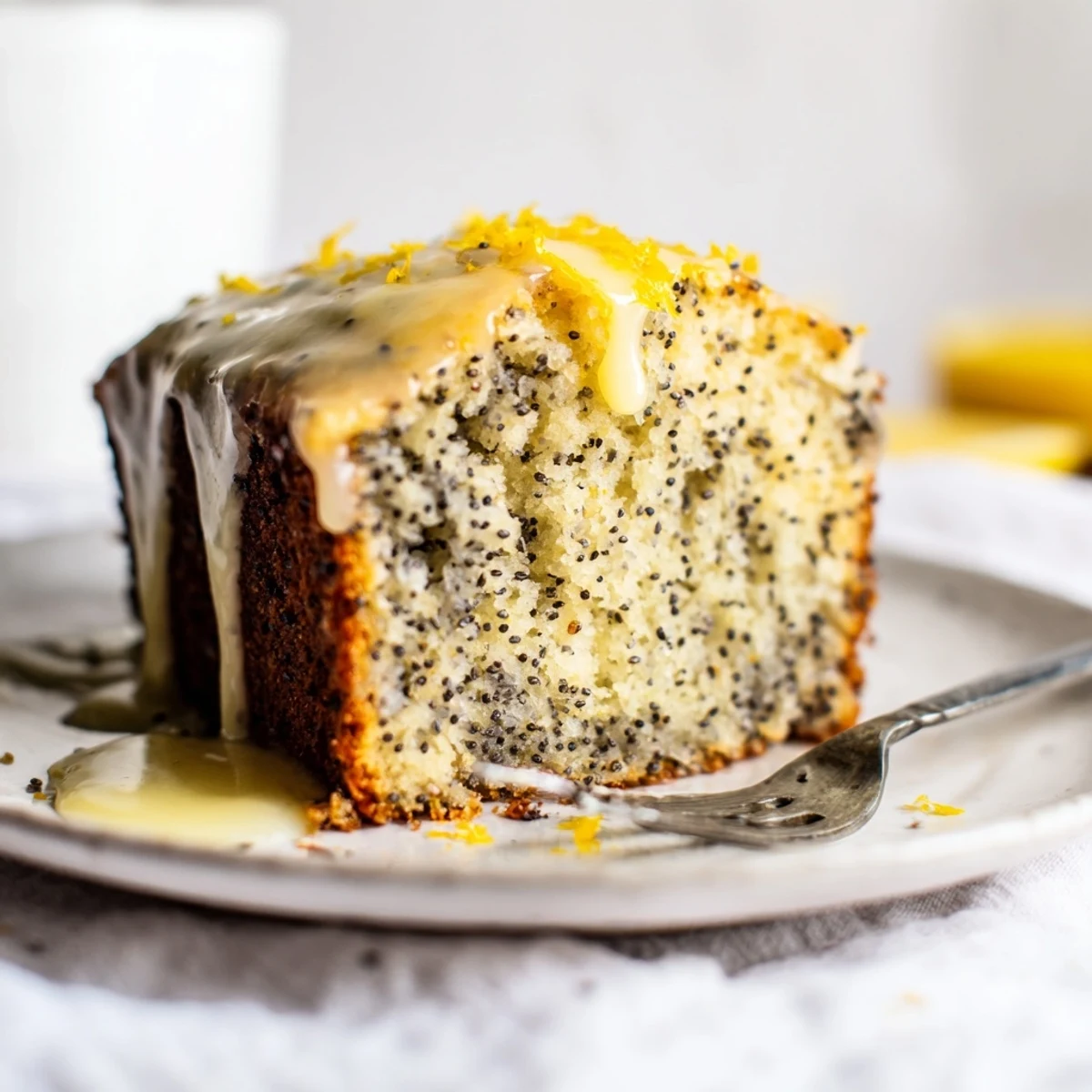 A glazed Lemon Poppy Seed Loaf Cake rests on a rustic wooden board, cut to show its moist crumb.