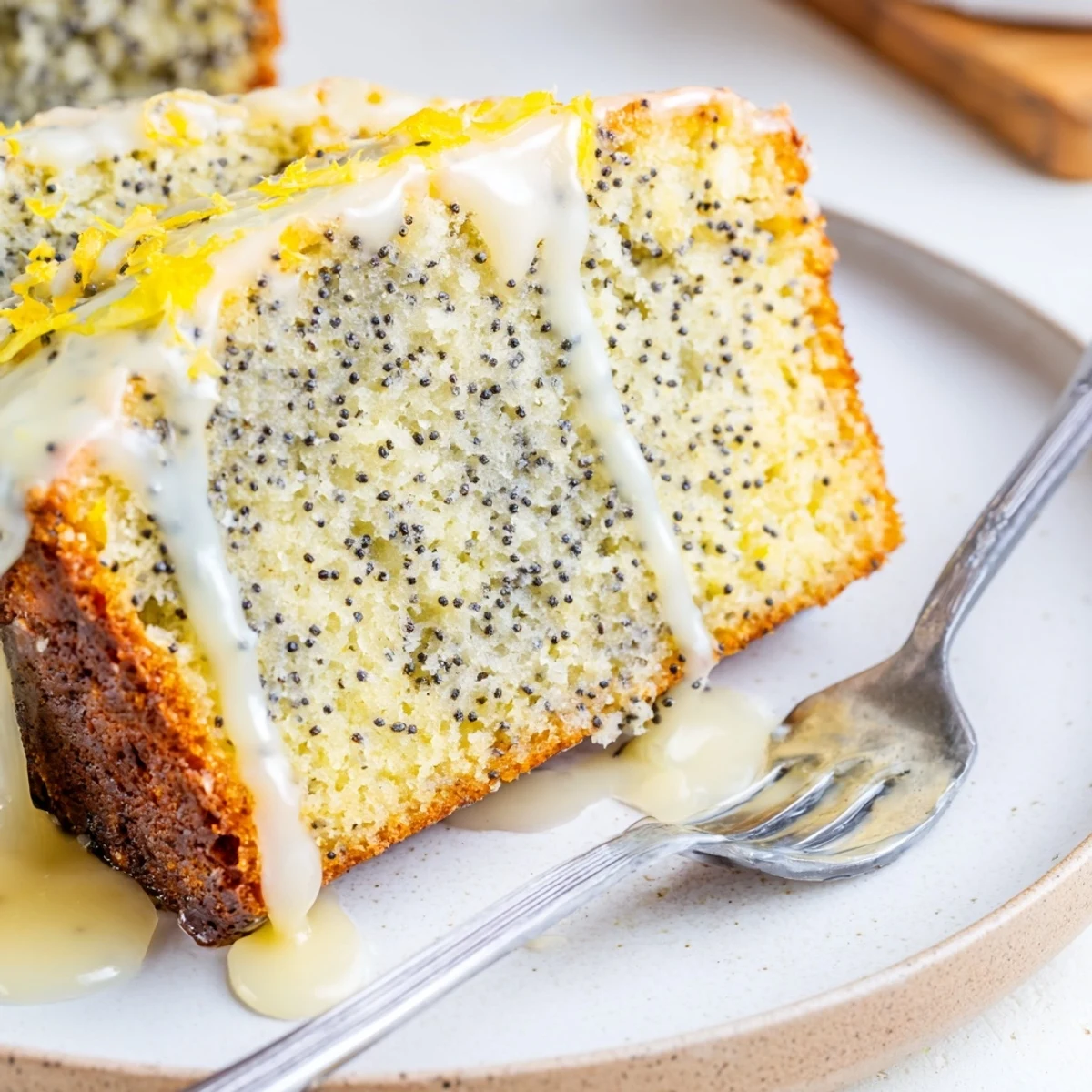 Slices of Lemon Poppy Seed Loaf Cake are plated with fresh lemon wedges and a hot cup of coffee nearby.