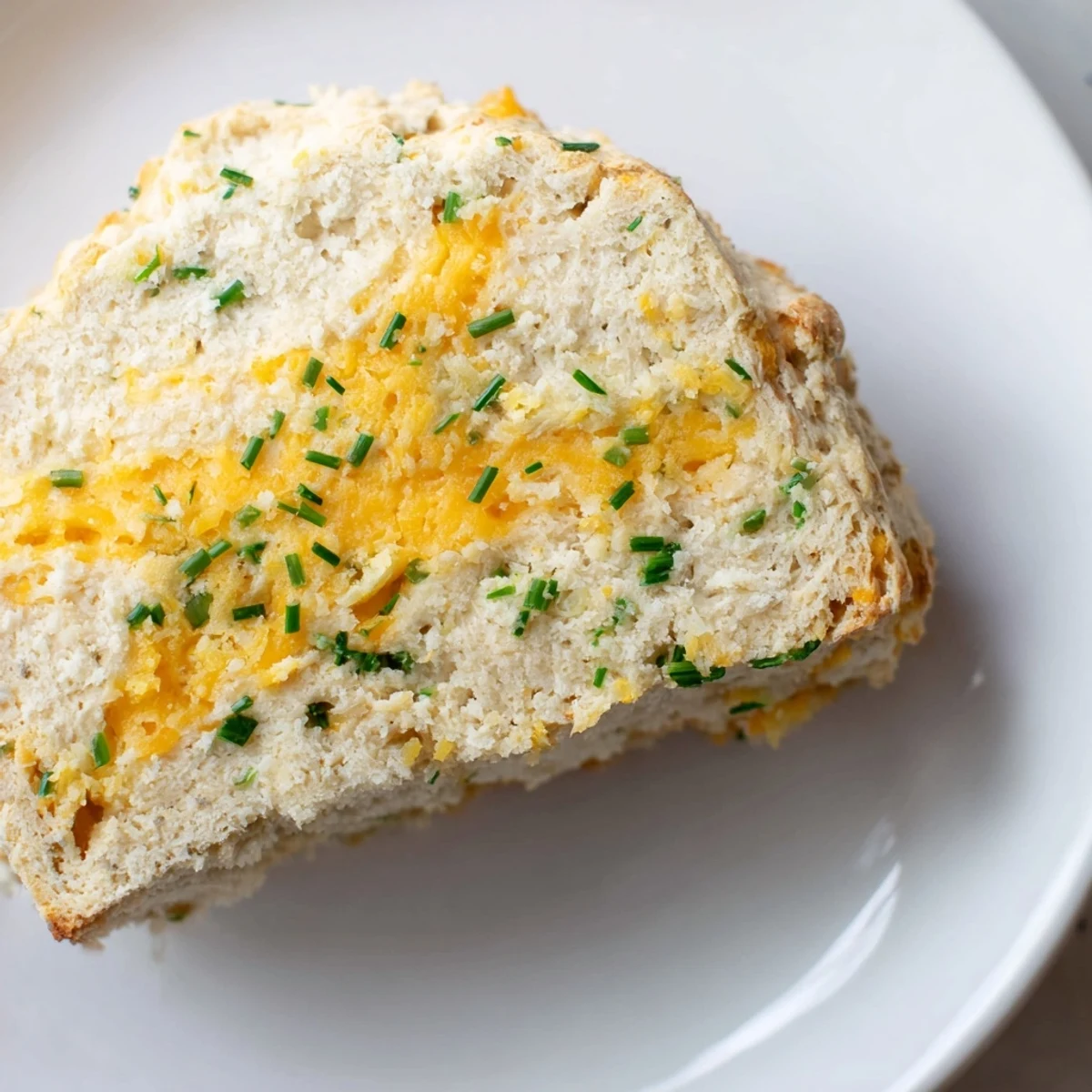 Slices of homemade Savory Cheddar & Chive Irish Soda Bread reveal a moist, tender interior studded with sharp cheddar and bright chives, ideal for a cozy dinner side or savory breakfast.