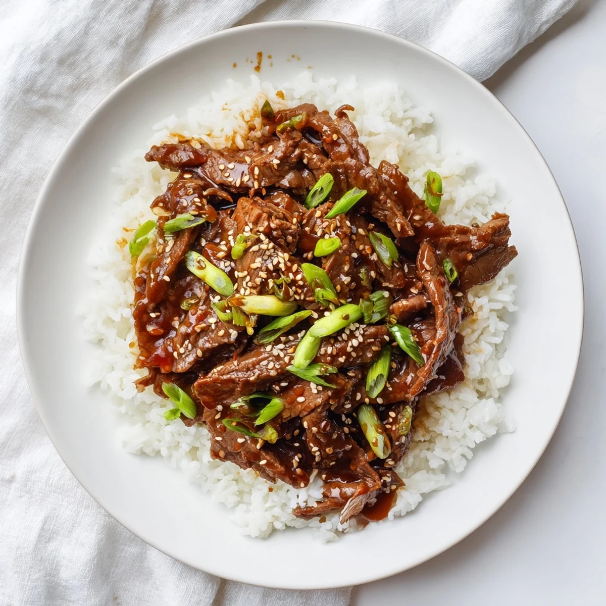 Ultimate Slow Cooker Mongolian Beef in a ceramic bowl, garnished with sesame seeds and fresh scallions.