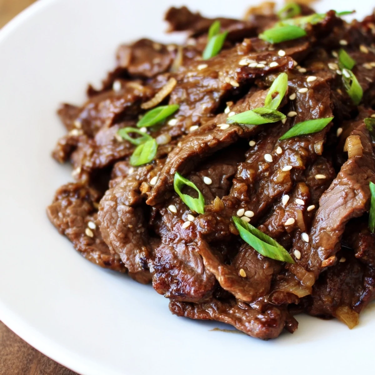 Tender slices of Ultimate Slow Cooker Mongolian Beef glisten in a savory-sweet sauce in a slow cooker.