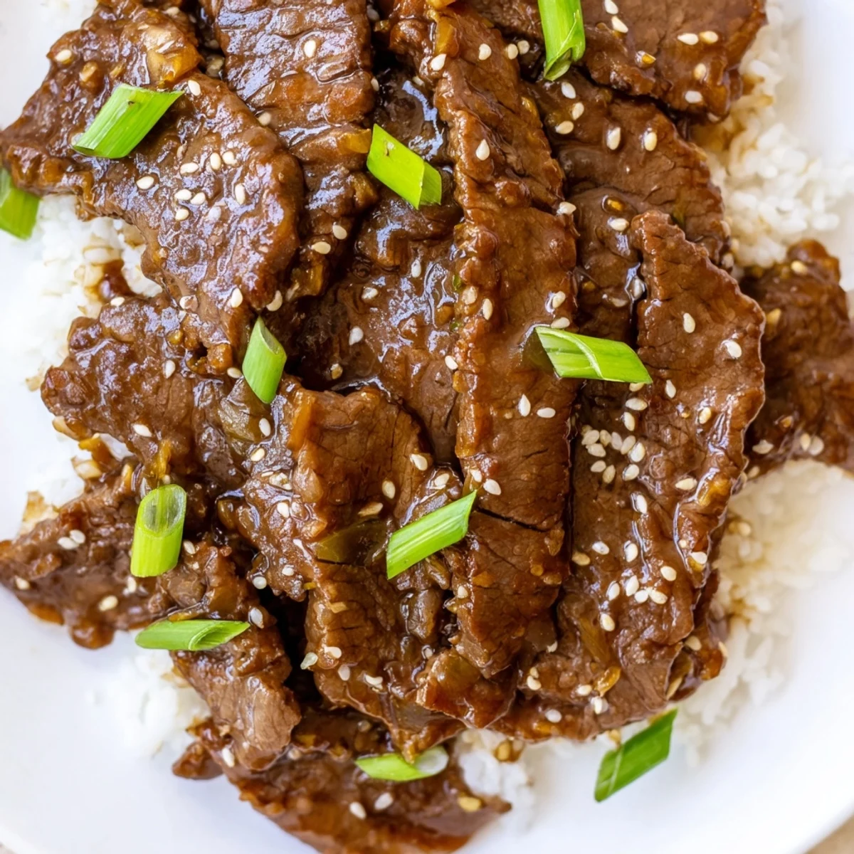 Close-up of Ultimate Slow Cooker Mongolian Beef garnished with sesame seeds and scallions on a dinner plate.