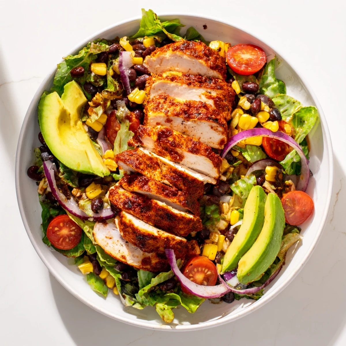 Hearty chipotle lime chicken salad is served in a rustic bowl, garnished with cherry tomatoes and red onion for color.