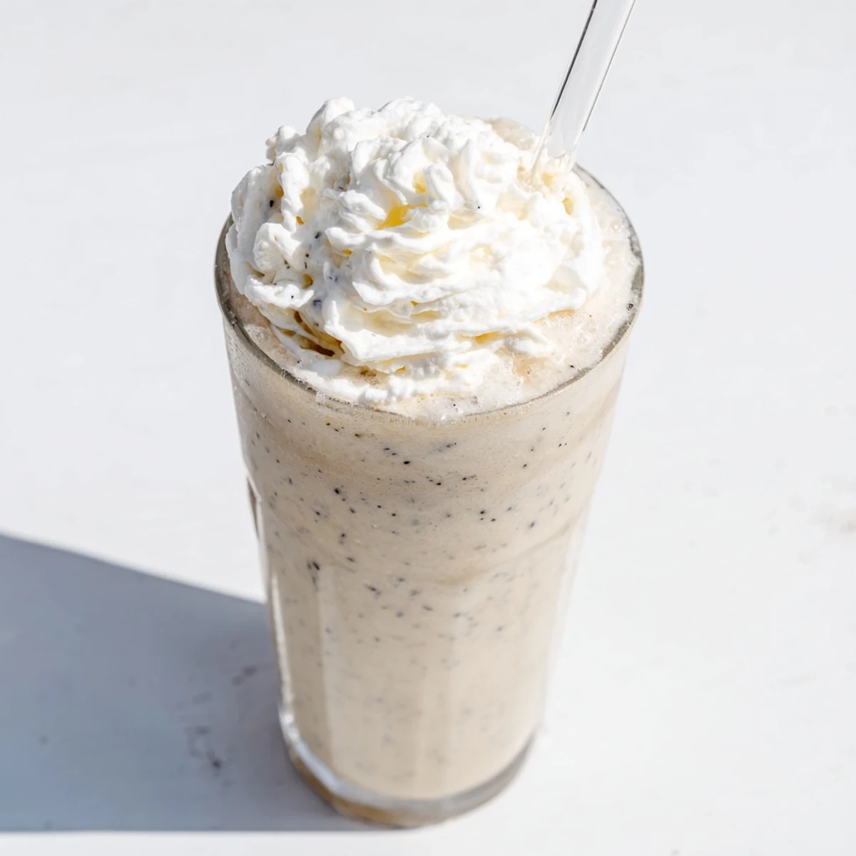 Two tall glasses of homemade Vanilla Bean Frappuccino topped with whipped cream beside a fresh vanilla bean pod.