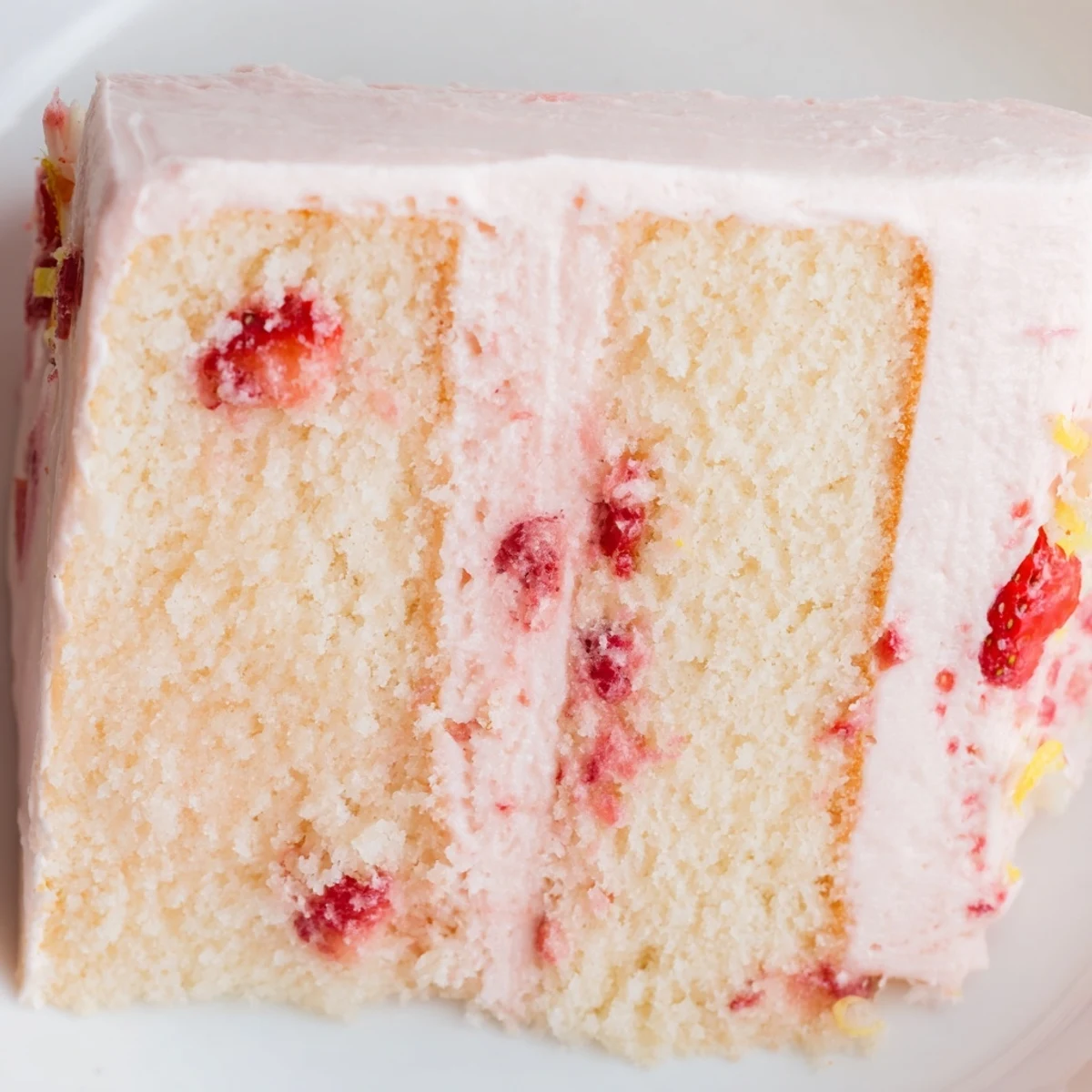 A close-up of Strawberry Lemonade Cake With Creamy Lemon Buttercream, showcasing moist pink layers and tangy lemon frosting with fresh strawberries on top.