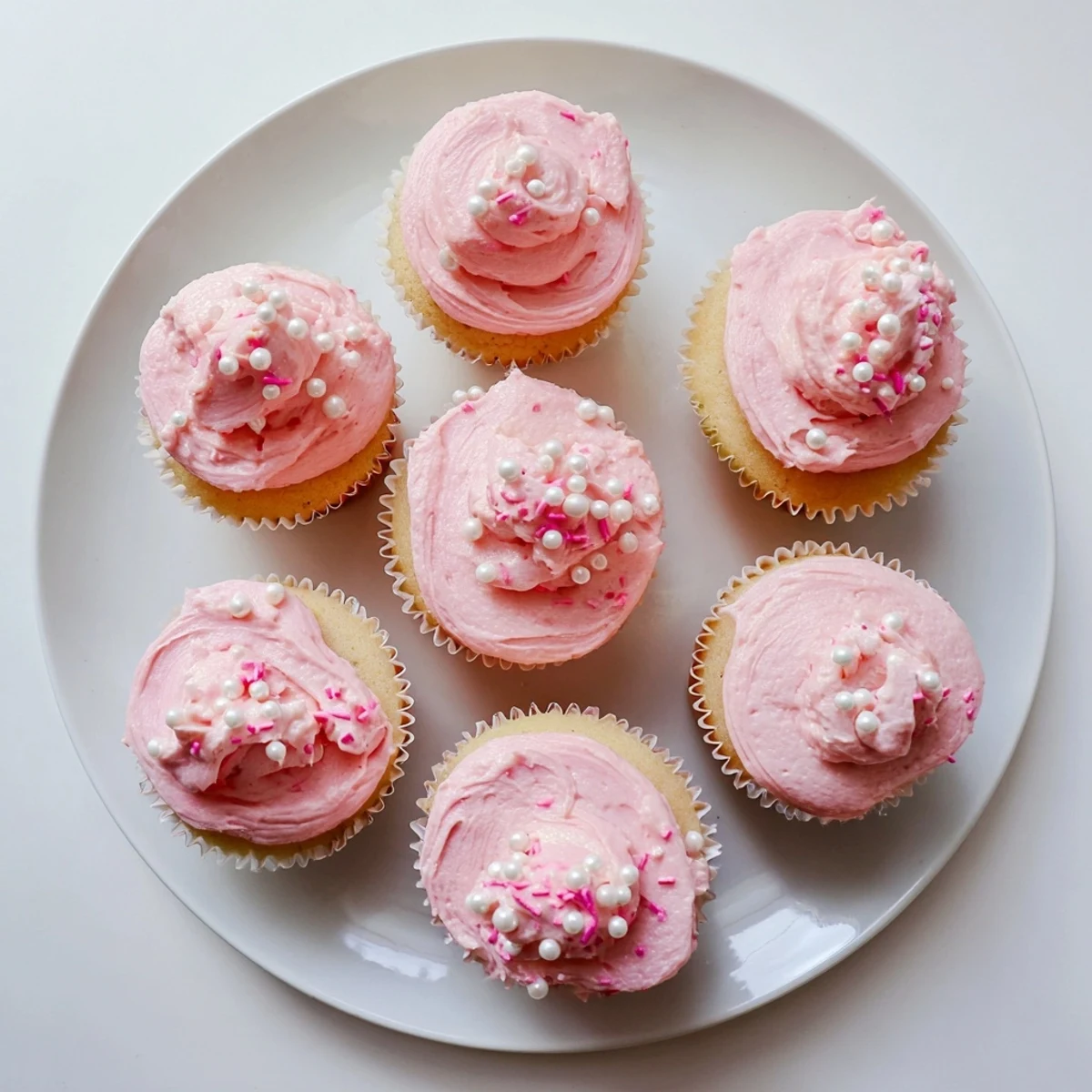 Freshly baked Girl Baby Shower Cupcakes in pastel liners with smooth swirls of pink frosting and delicate edible decor.
