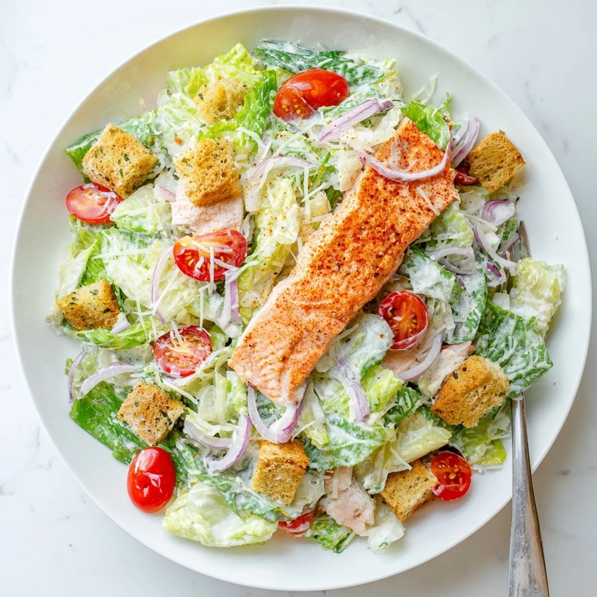 Bright cherry tomatoes and shaved Parmesan garnish a freshly tossed Salmon Caesar Salad served on a white plate for lunch.