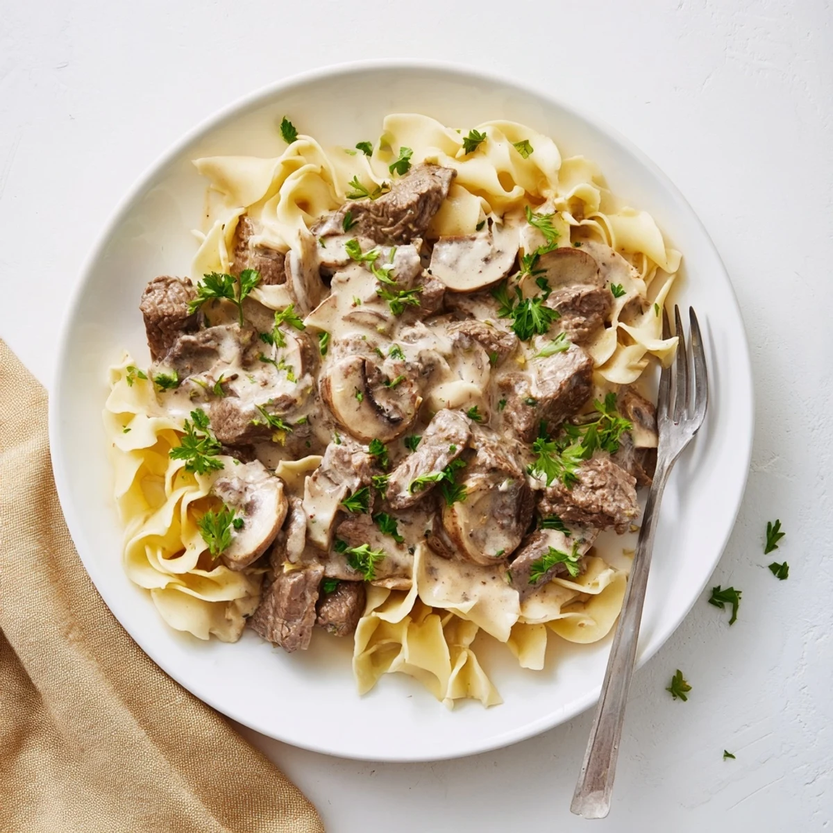 Homemade beef and mushroom stroganoff plated over wide egg noodles with chopped parsley topping