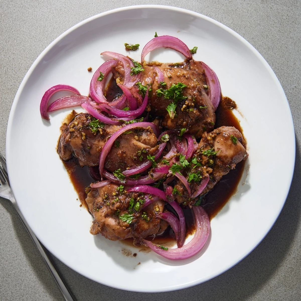 Slow cooker balsamic chicken with glazed thighs resting over caramelized red onions and fresh parsley garnish