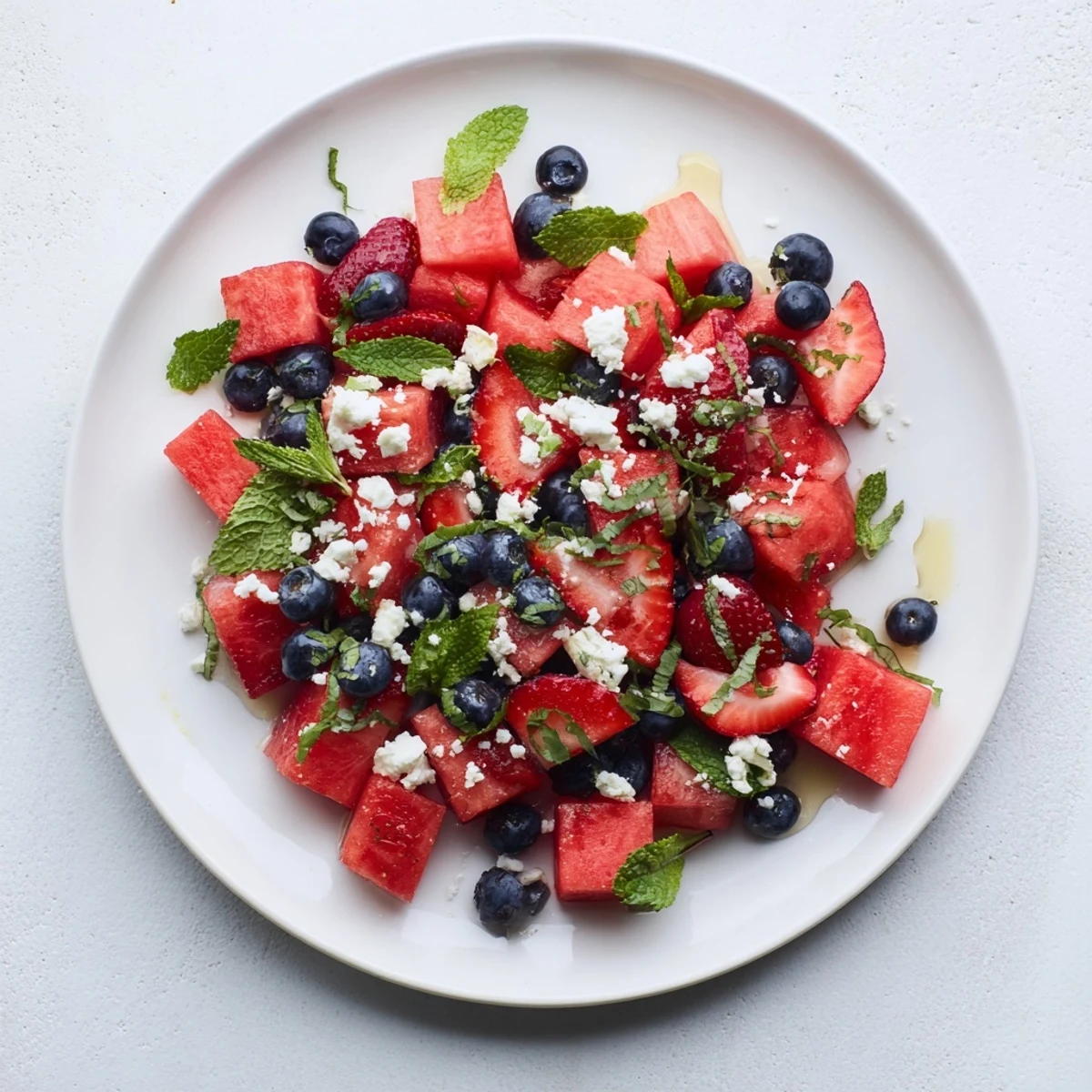 Vibrant summer strawberry watermelon salad drizzled with tangy honey lime dressing on a rustic wooden serving board
