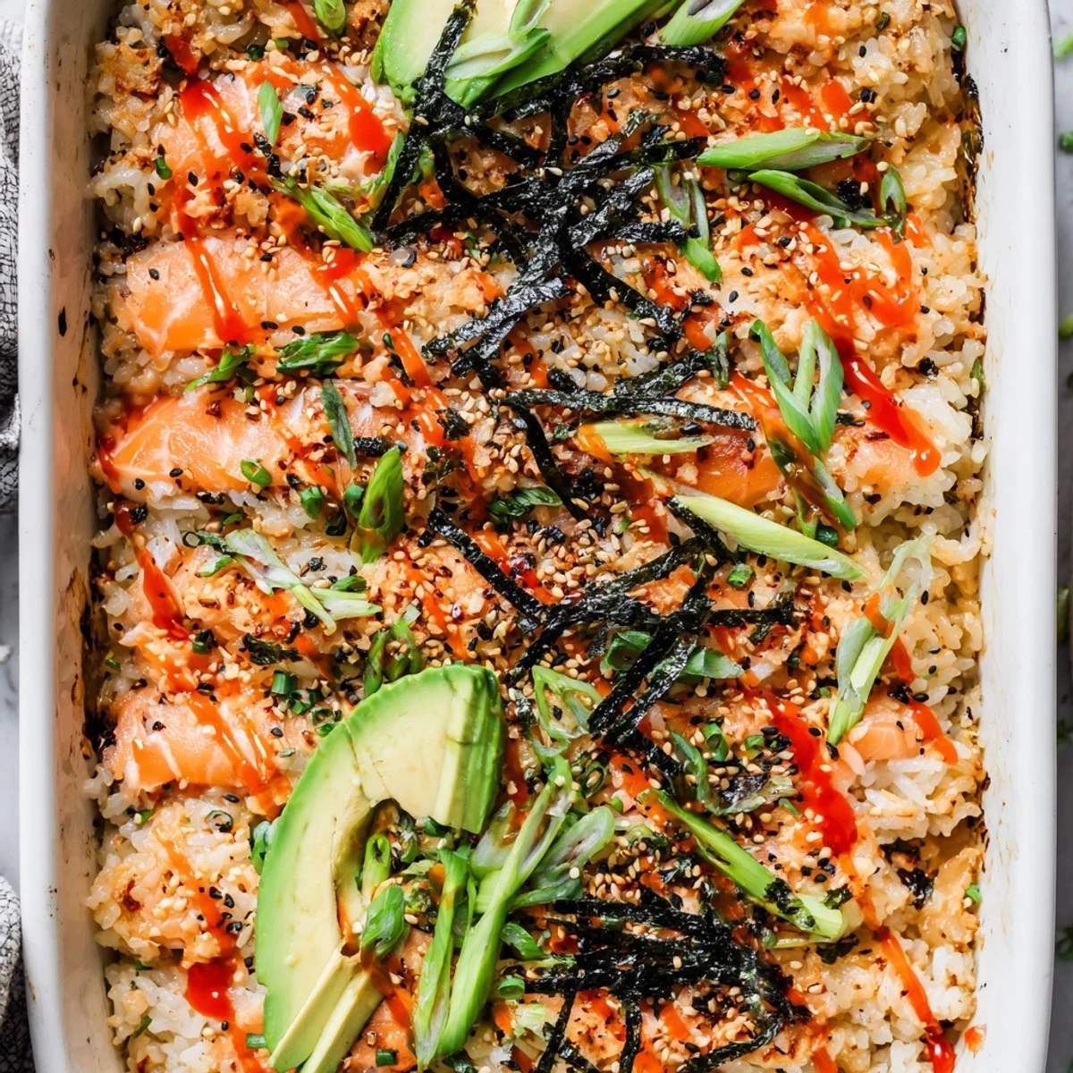 Golden salmon sushi bake casserole with fluffy seasoned rice, spicy mayo, and fresh avocado slices