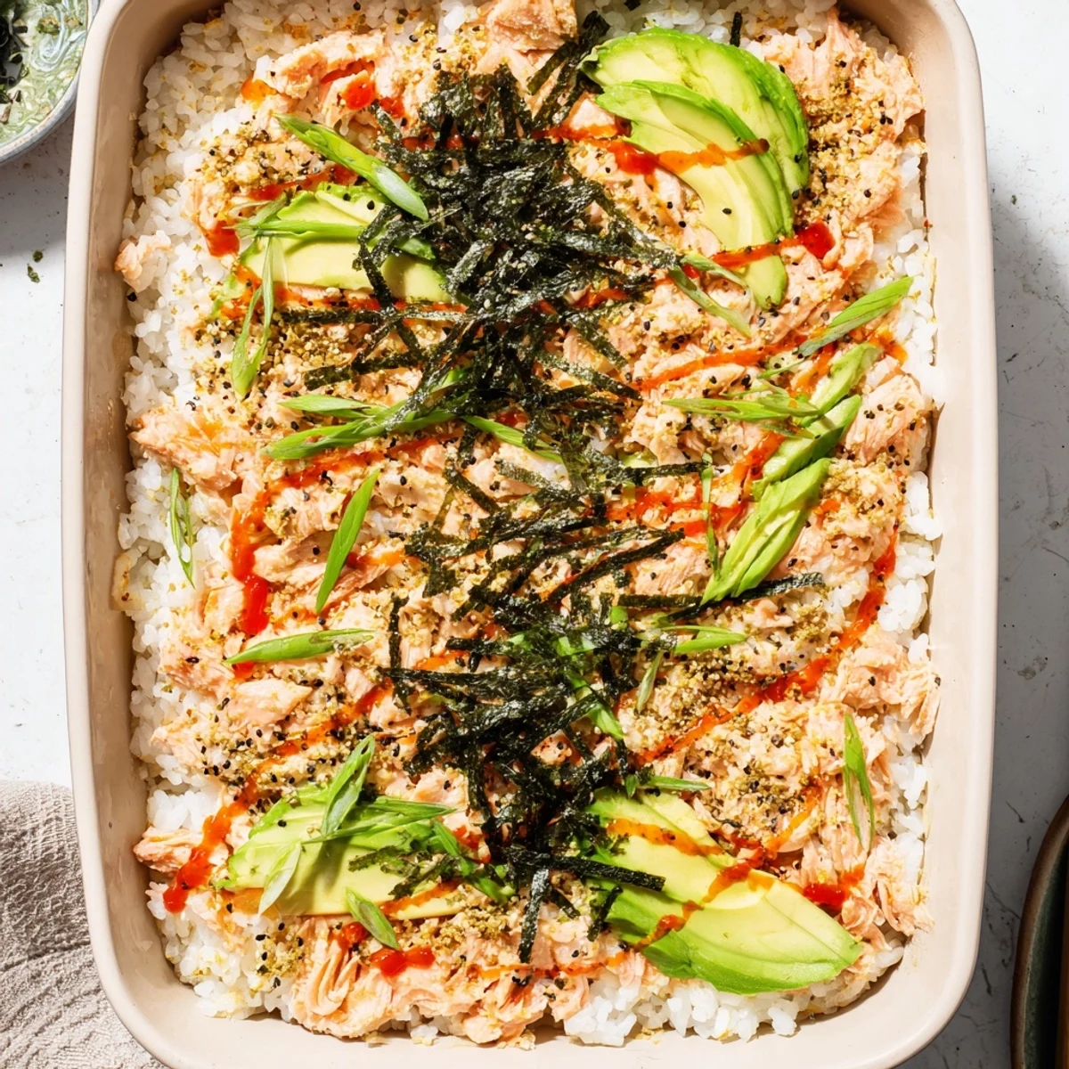 Warm deconstructed salmon sushi bake topped with nori strips, green onions, and toasted sesame seeds