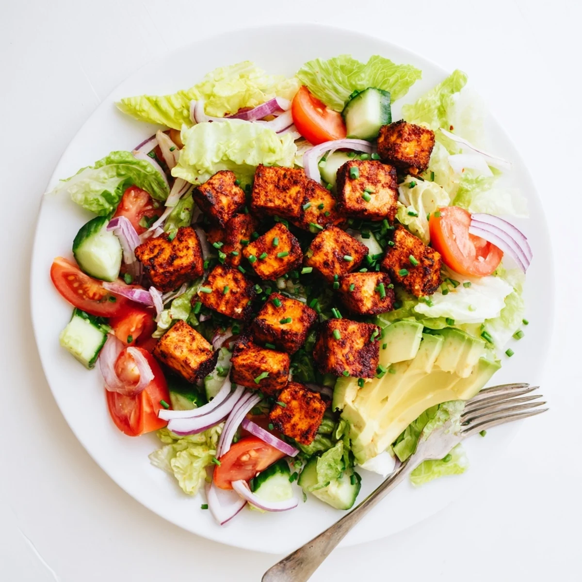 Golden smoky tofu cubes atop crisp lettuce and juicy ripe tomato slices in a summer salad bowl