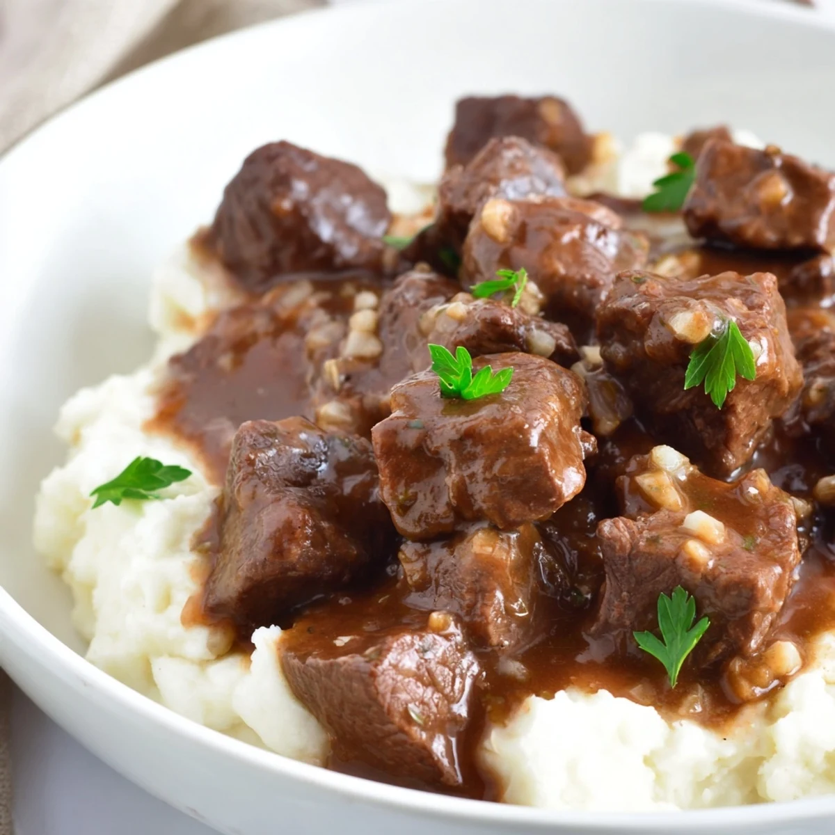 Tender slow cooker beef tips and gravy served over creamy mashed potatoes with fresh parsley garnish