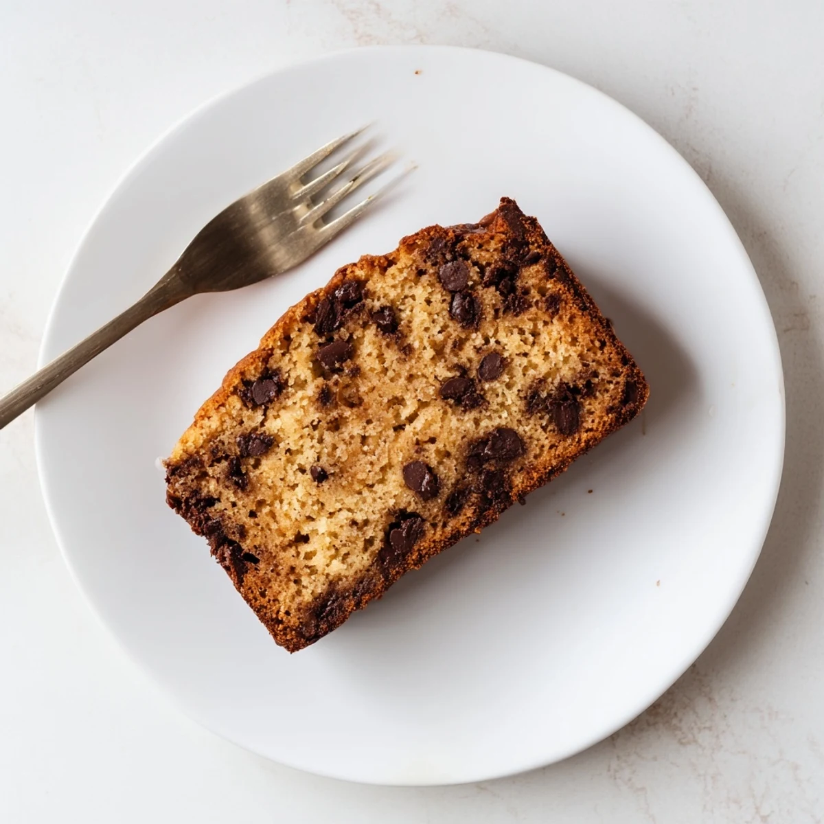 Golden chocolate chip banana bread loaf with melted chips on a rustic wooden board