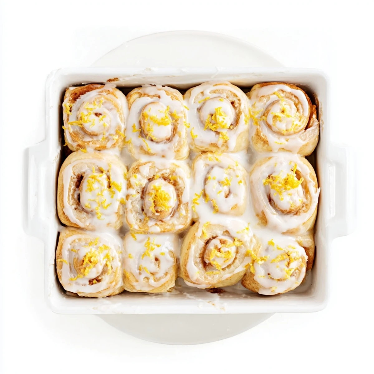 Golden homemade lemon rolls drizzled with white glaze and fresh lemon zest on a serving plate