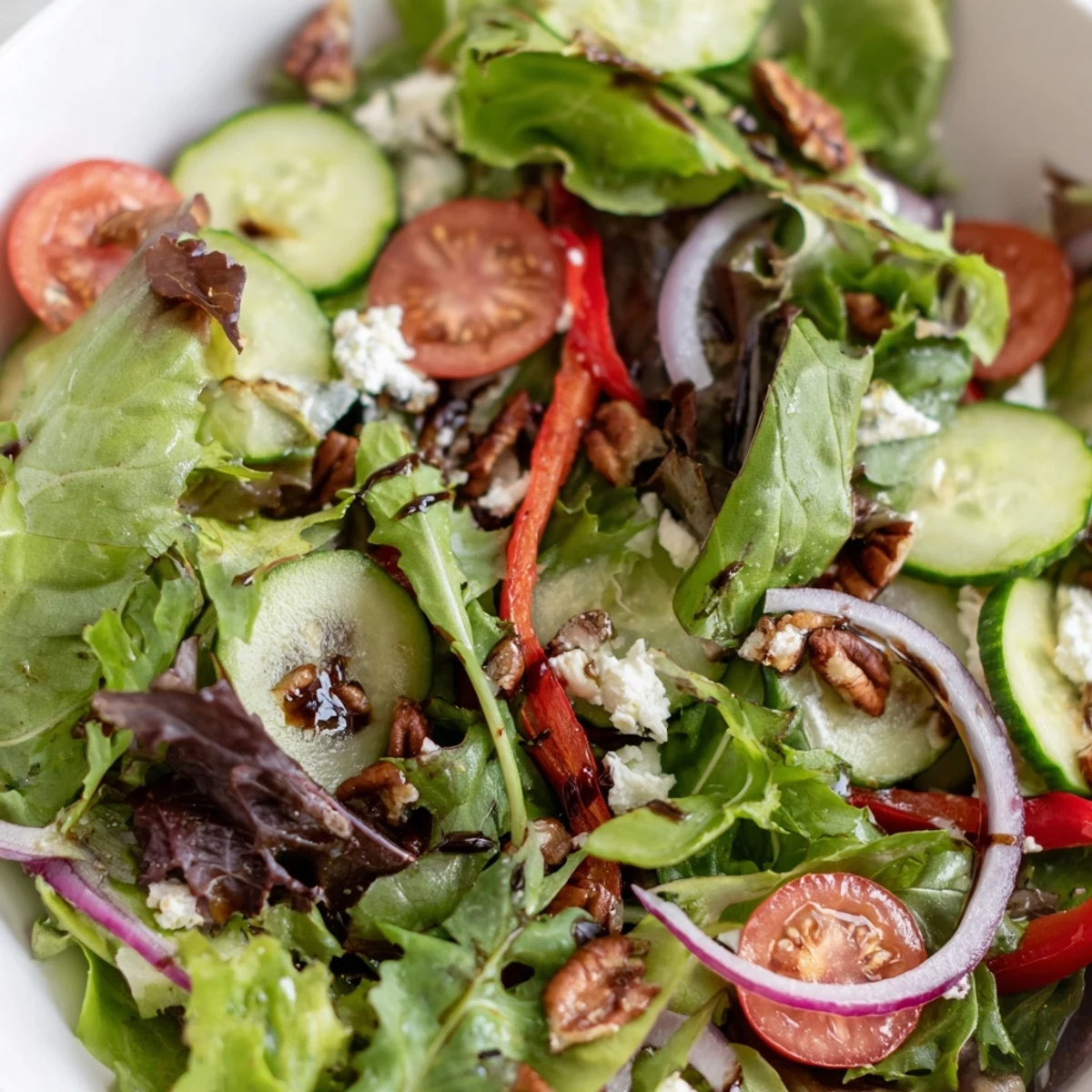 A vibrant spring mix salad topped with cherry tomatoes, cucumber, and crumbled feta cheese