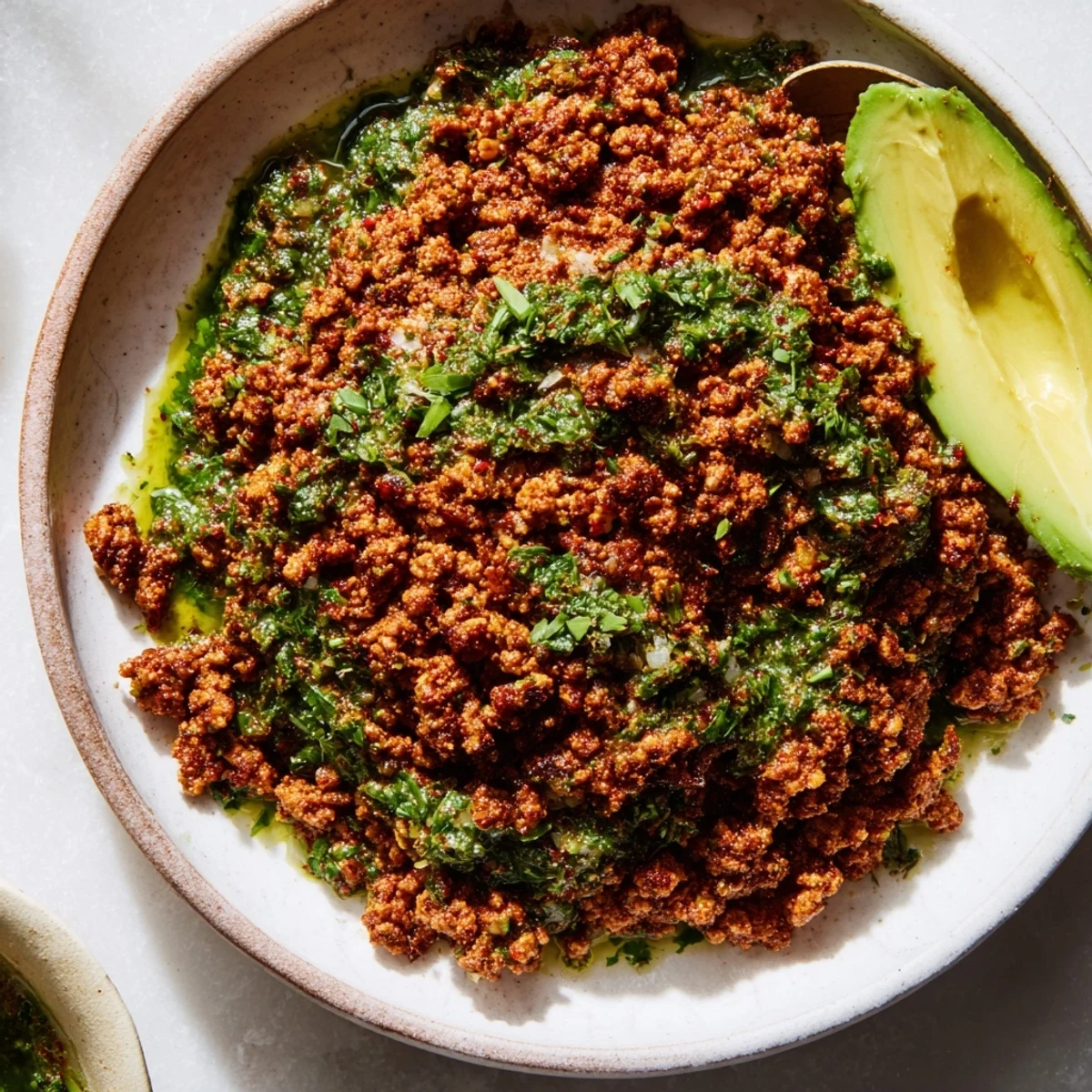 Zesty chimichurri sauce drizzled over spiced ground beef with avocado slices and colorful veggies in bowl