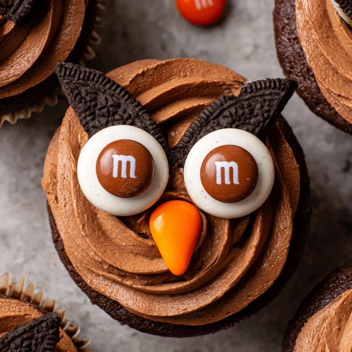 Cute Oreo Owl Cupcakes topped with chocolate frosting and candy eyes on a rustic serving plate