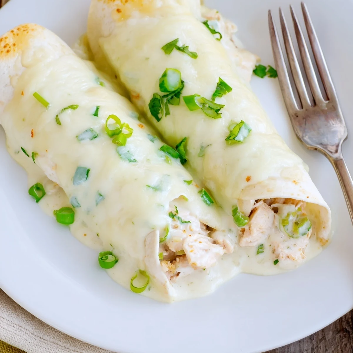 Plate of Creamy White Chicken Enchiladas steaming, cheesy filling peeking through tortillas