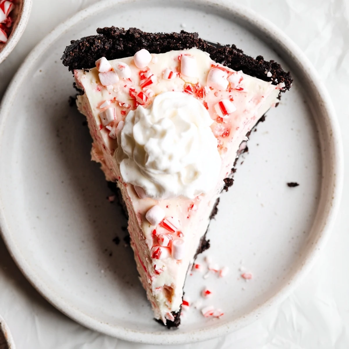 Slice of Candy Cane Pie on plate, fluffy whipped topping and crunchy peppermint bits
