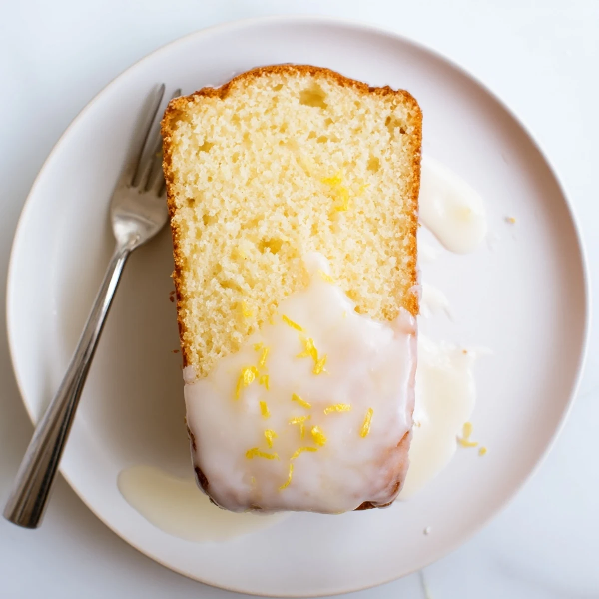 Golden Greek yogurt lemon loaf drizzled with white glaze on a wooden cutting board