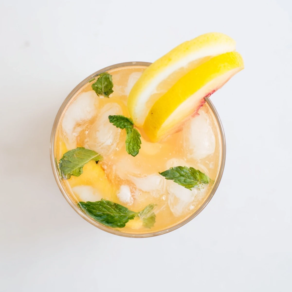 Golden fresh peach lemonade in a glass pitcher garnished with mint leaves