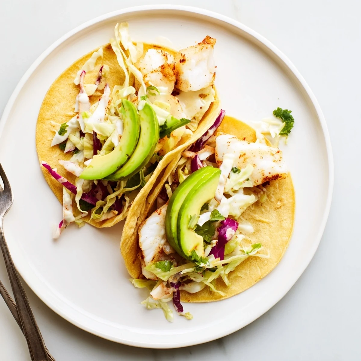 Baked Cod Fish Tacos with Creamy Cilantro Lime Sauce, topped with sliced avocado