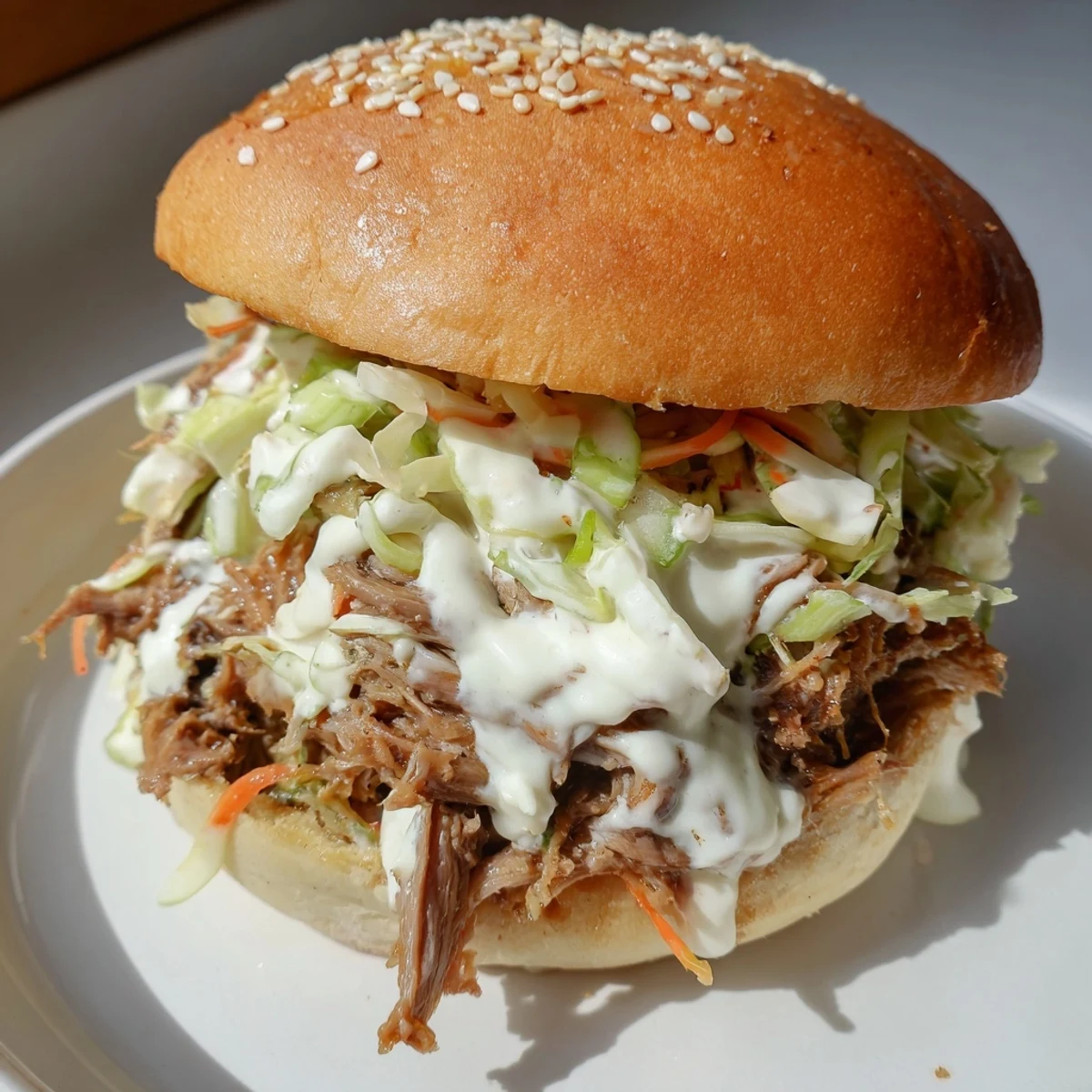Tender shredded lamb shoulder glistening with tangy Alabama white sauce on soft golden slider buns