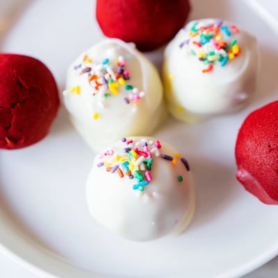 Deep red cake balls coated in glossy white chocolate, ready to serve as handheld treats on festive dessert tables.