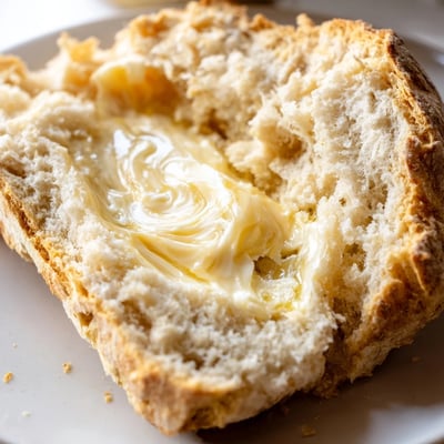 Golden-brown Irish Soda Bread loaf, cut to reveal its fluffy interior, served with a thick pat of creamy Irish butter melting on top.
