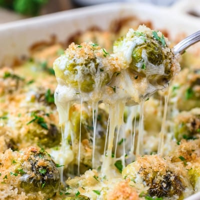 Tender halved Brussels sprouts baked in rich cheesy Parmesan sauce served in a white casserole dish