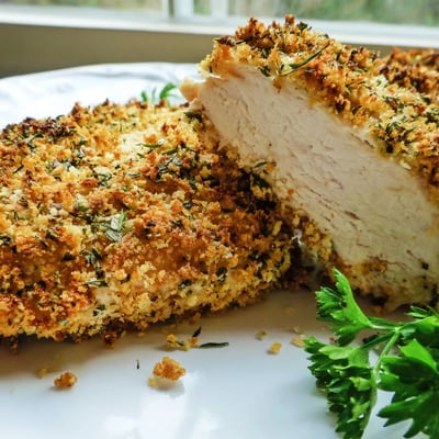 Juicy savory herbed Parmesan chicken garnished with fresh parsley and lemon wedges